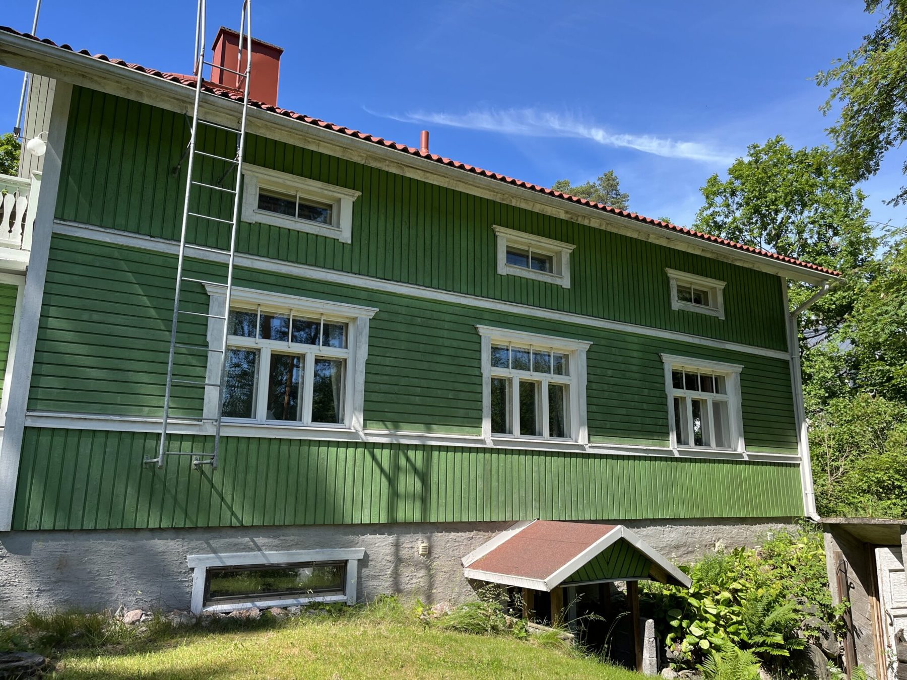 Kaksikerroksisen puutalon pitkä räystäs, vesikouru ja syöksytorvi kesällä